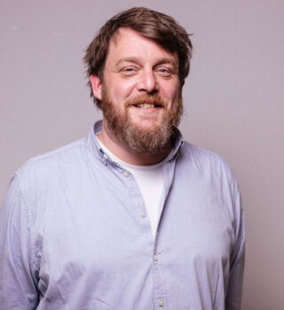 Portrait eines Mannes mit einem Bart in einem hellblauen Hemd, der in die Kamera lacht. Der Mann heißt Carsten Bohlken und ist die Leitung von der Wohnstätte Barkel.
