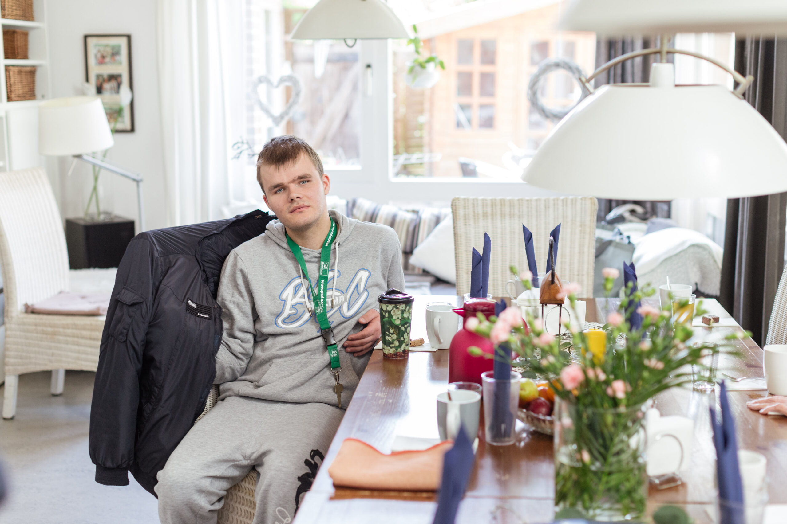 In einem Gemeinschaftsraum in der Wohnstätte Tannenhof. Ein junger Bewohner sitzt an einem Tisch und schaut in die Kamera.
