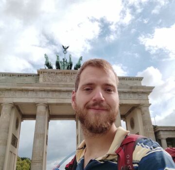 Ein junger Mann namens Jan Kleen steht draußen in Berlin vor dem Brandenburger Tor. Er schaut freundlich.