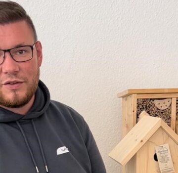 Ein GPS Mitarbeiter namens Marcel Menze steht vor der Kamera. Er schaut freundlich. Im Hintergrund ist ein Vogelhaus und ein Insektenhotel aus Holz zu sehen.