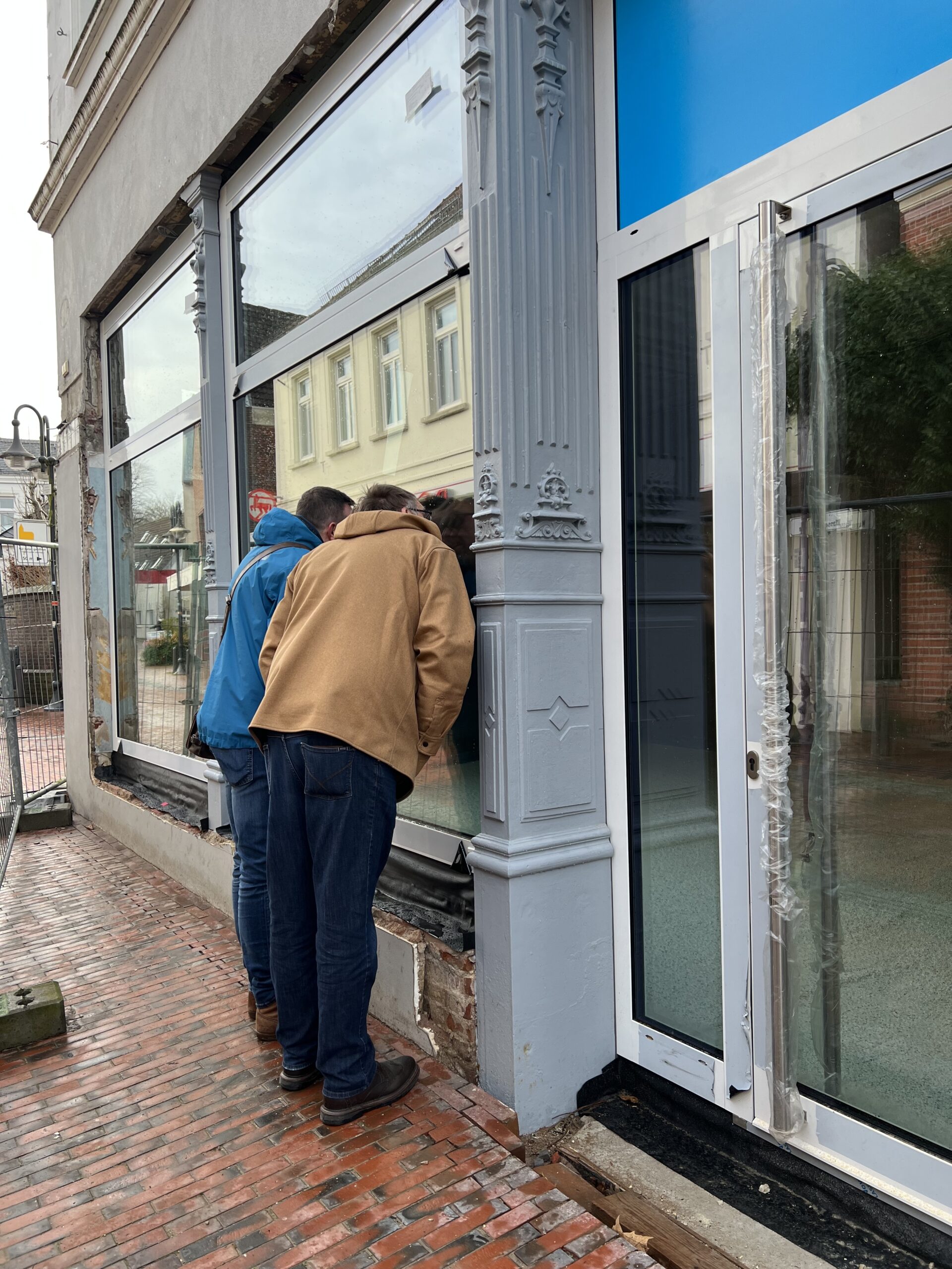 GPS Geschäftsführer Klaus Puschmann und ein GPS Mitarbeiter schauen durchs Fenster in das Innere des GPS Ladens "Nordseefreundlich".