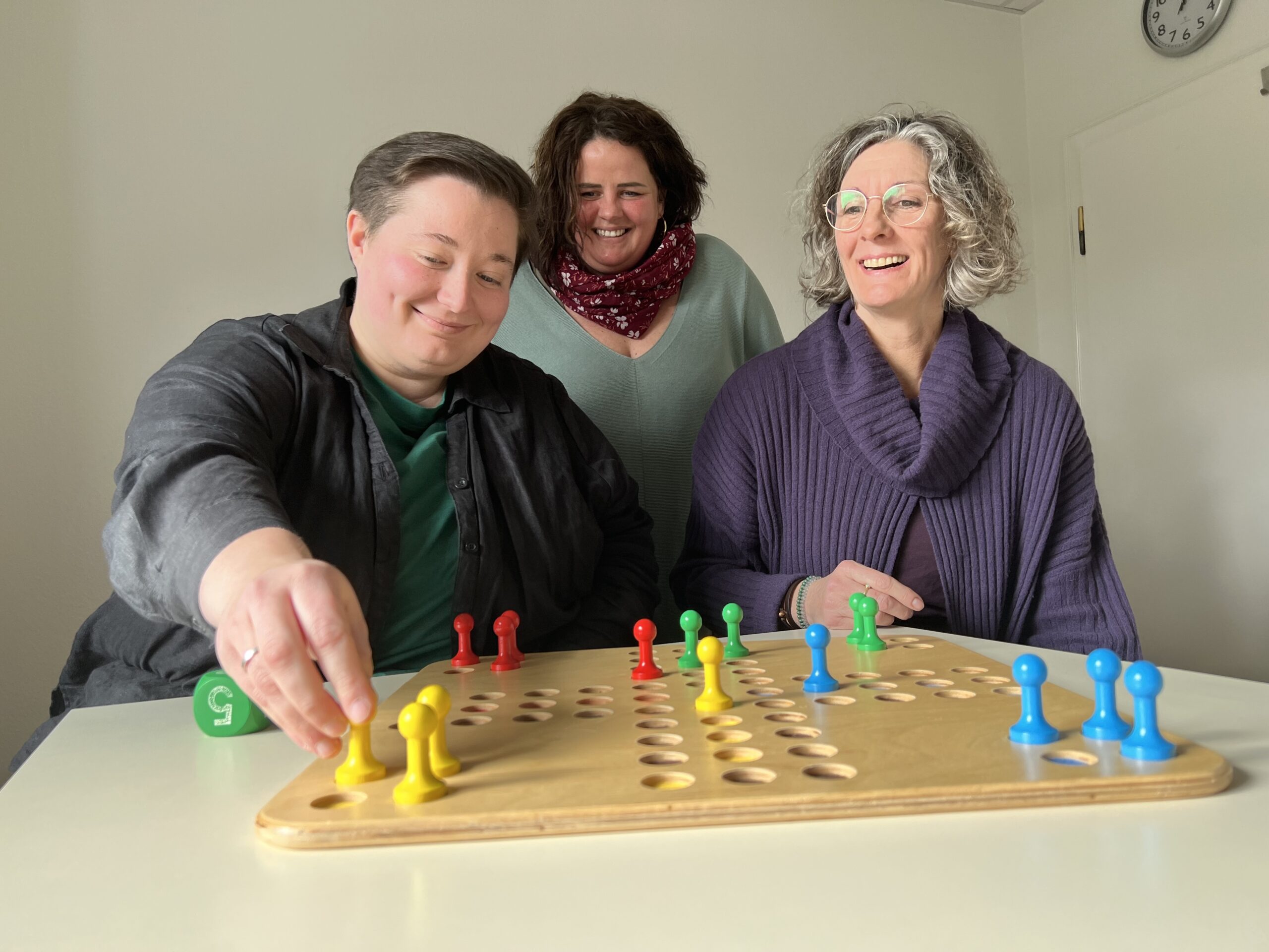 Drei Frauen spielen an einem Tisch das Spiel "Mensch ärgere Dich nicht".
