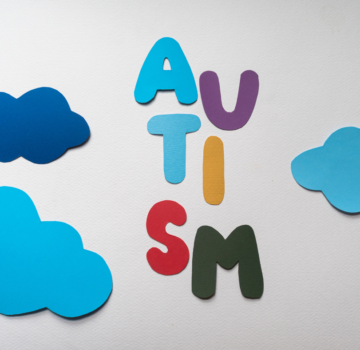 Drei blaue Wolken aus Papier und sechs Buschstaben aus Papier, das zusammen als Wort "Autism" gelesen wird. Es heißt von Englisch auf Deutsch "Autismus".