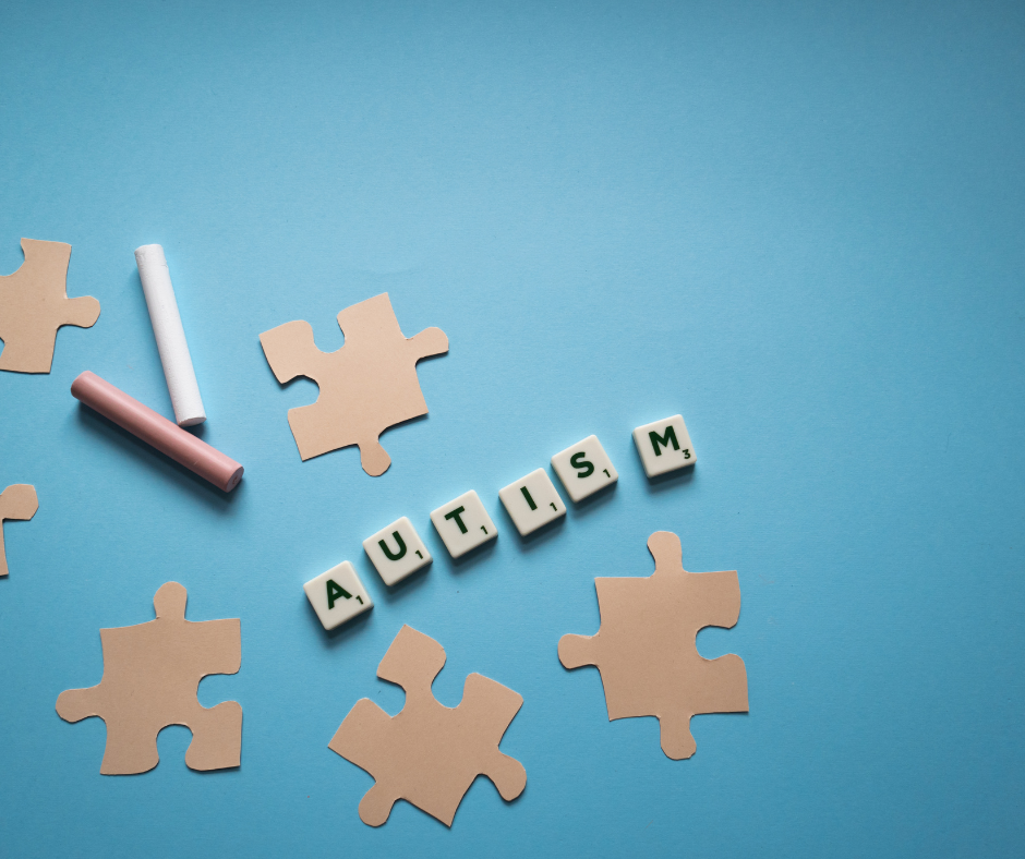 Kleine braune Puzzleteile aus Papier, zwei verschiedene, farbige Wachsmalstifte und jeweils sechs weiße kleine Würfel mit Buchstaben. Die weißen Würfel ergeben das englische Wort für "Autism", das auf Deutsch "Autismus" heißt.