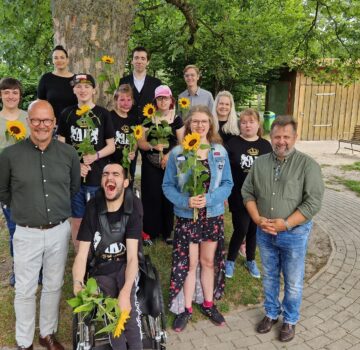 Man sieht junge Schüler von der Dorfschule Mansie und den Schulleiter Friedrich Fittje mit den Lehrern draußen im Garten bei Ihrer Verabschiedung. Die Schüler halten eine Sonnenblume in der Hand.