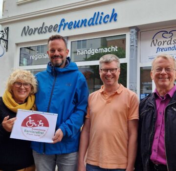 Zwei Frauen und drei Männer stehen draußen vor dem GPS Laden "Nordseefreundlich". Ein Mann und eine Frau halten einen Zettel, wo darauf steht "Auszeichnung Barrierefrei Projekt Sophie".