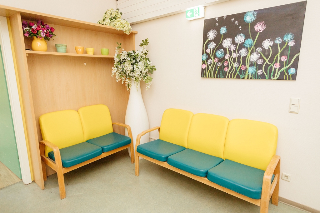 Man erkennt einen Raum mit zwei Sofas in den Farben gelb/ grün. Ein Bild mit Blumen und weitere Dekoration hängt an der Wand.