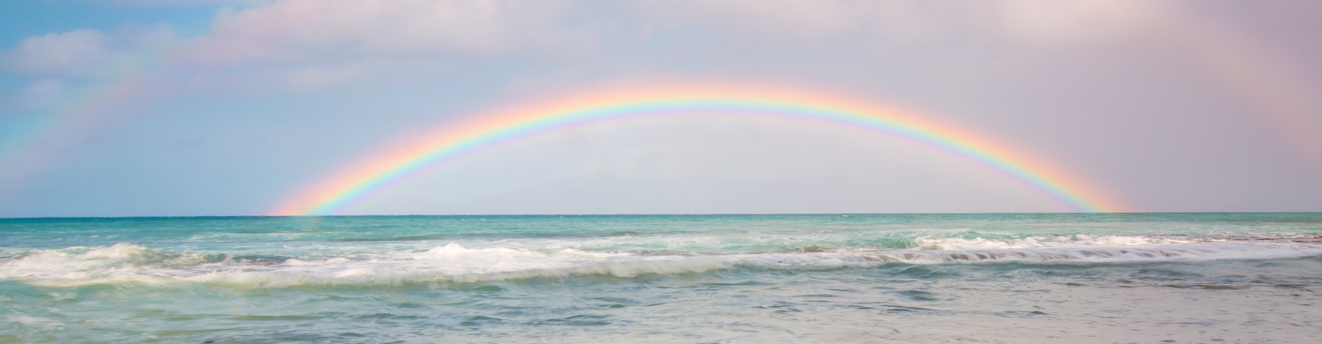 Ein blau und lila farbiger Himmel. Man sieht auch einen Regenbogen und das Meer.