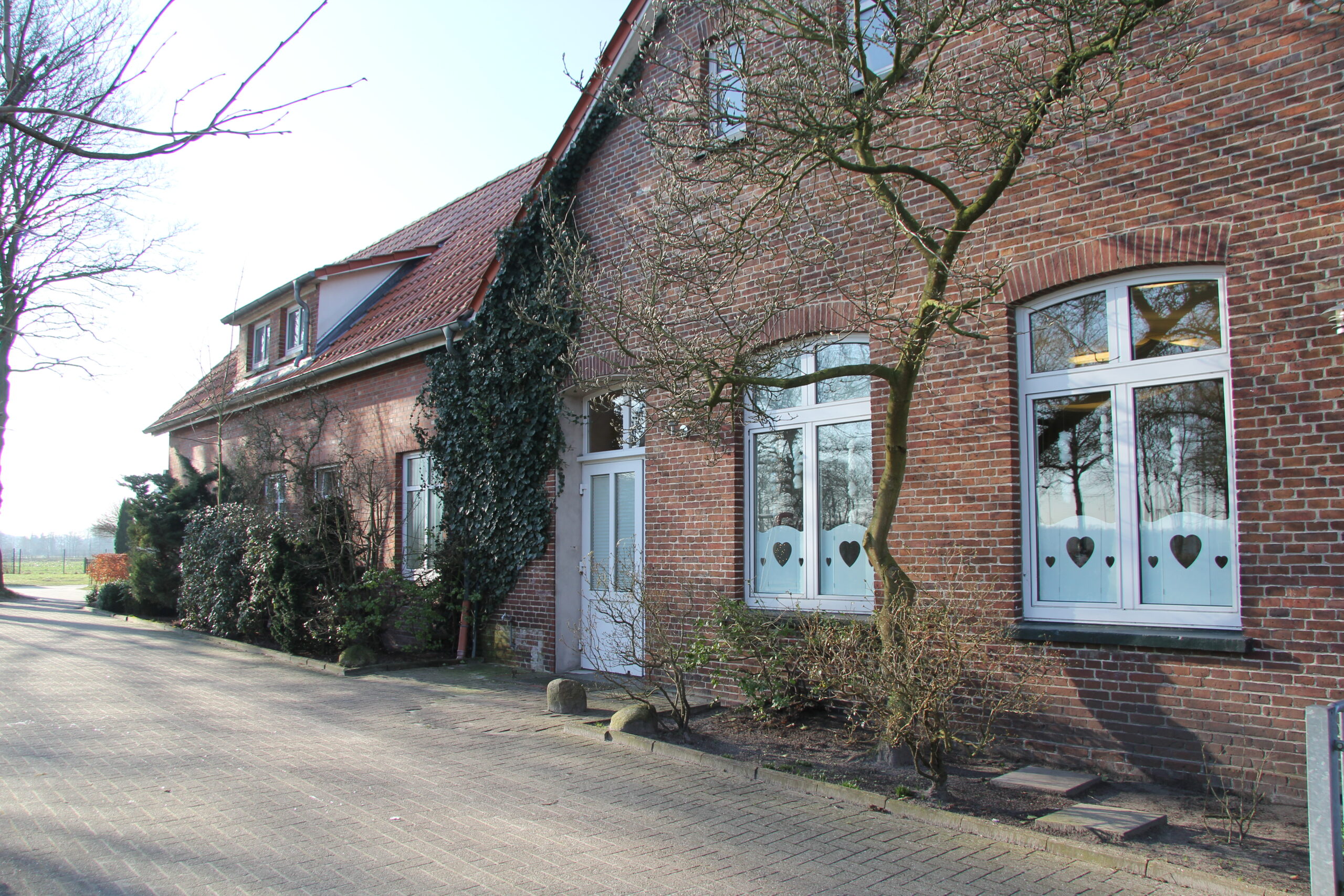 Man sieht ein rotes langes Haus. Man sieht einen Vorgarten draußen