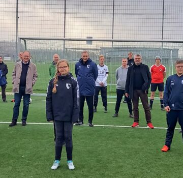 Man sieht Erwachsene und Kinder vor einem Fußballtor und auf einen Fußballfeld