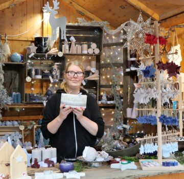 Einen Stand mit einer jungen Frau mit weihnachtlichen gebastelten Geschenken (zum Beispiel Glöckchen mit Bänder, Tannenbaum und Häuser aus Holz, Wachskerzen, usw.) Geschenkartikel von der GPS Werkstatt Jeringhave