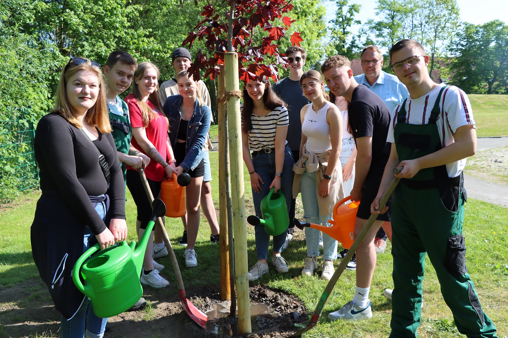 Eine Gruppe von FSJlern stehen vor dem gepflanzten Baum. Sechs von ihnen haben eine Schaufel und eine Gießkanne