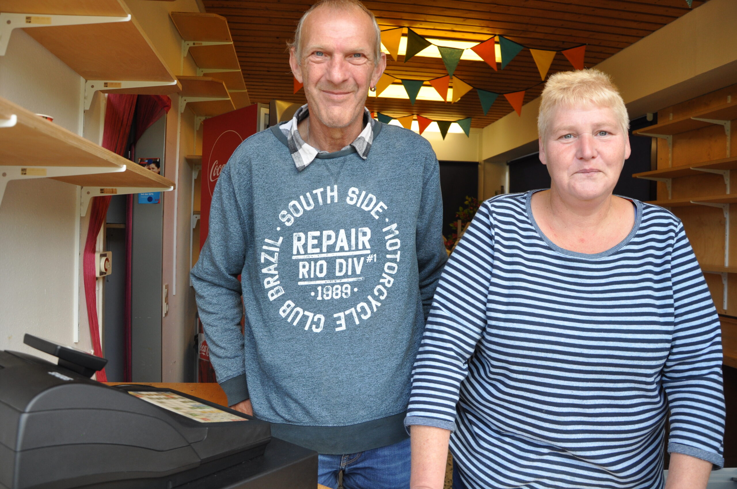 Zwei Mitarbeiter des GPS Kiosks. Ein Mann und eine Frau stehen vor der Kamera. Sie schauen freundlich.