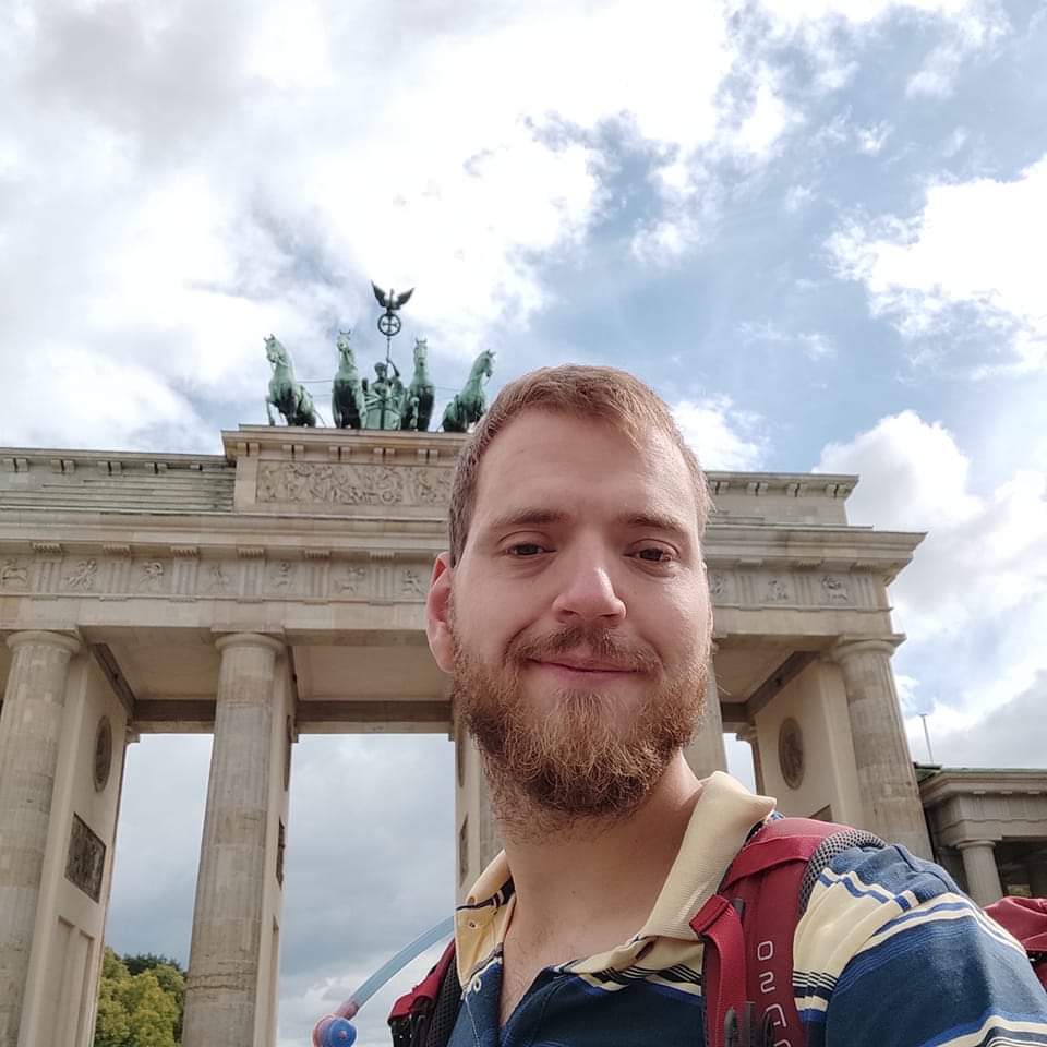 Ein junger Mann namens Jan Kleen steht draußen in Berlin vor dem Brandenburger Tor. Er schaut freundlich.