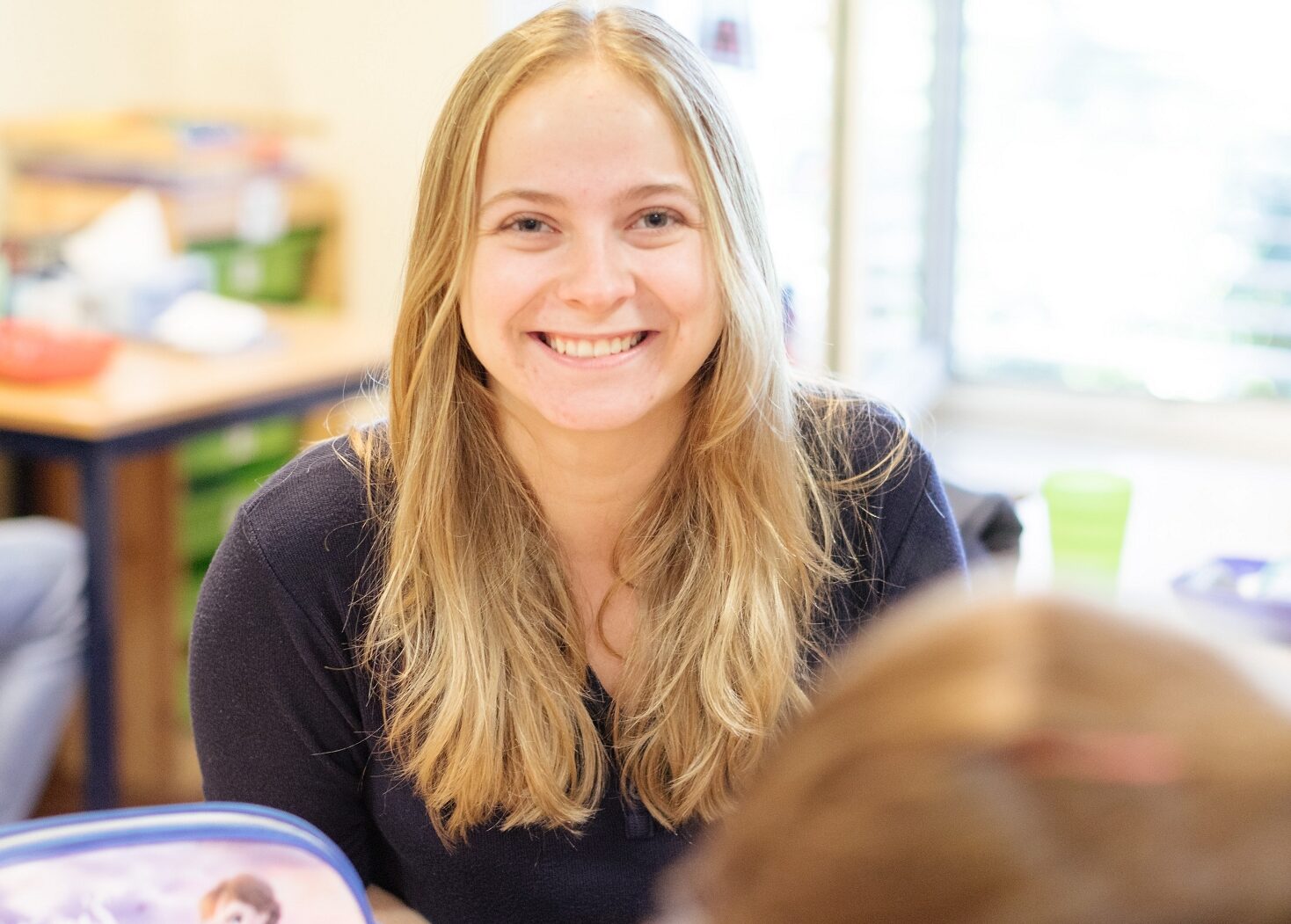 Eine junge Frau sitzt an einem Tisch. Sie ist mit anderen Kindern in einem Klassenraum.