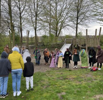 Viele junge Menschen sind draußen auf einem Spielplatz. Sie sind alle mit unterschiedlichen Kostümen für ein Theaterstück verkleidet.