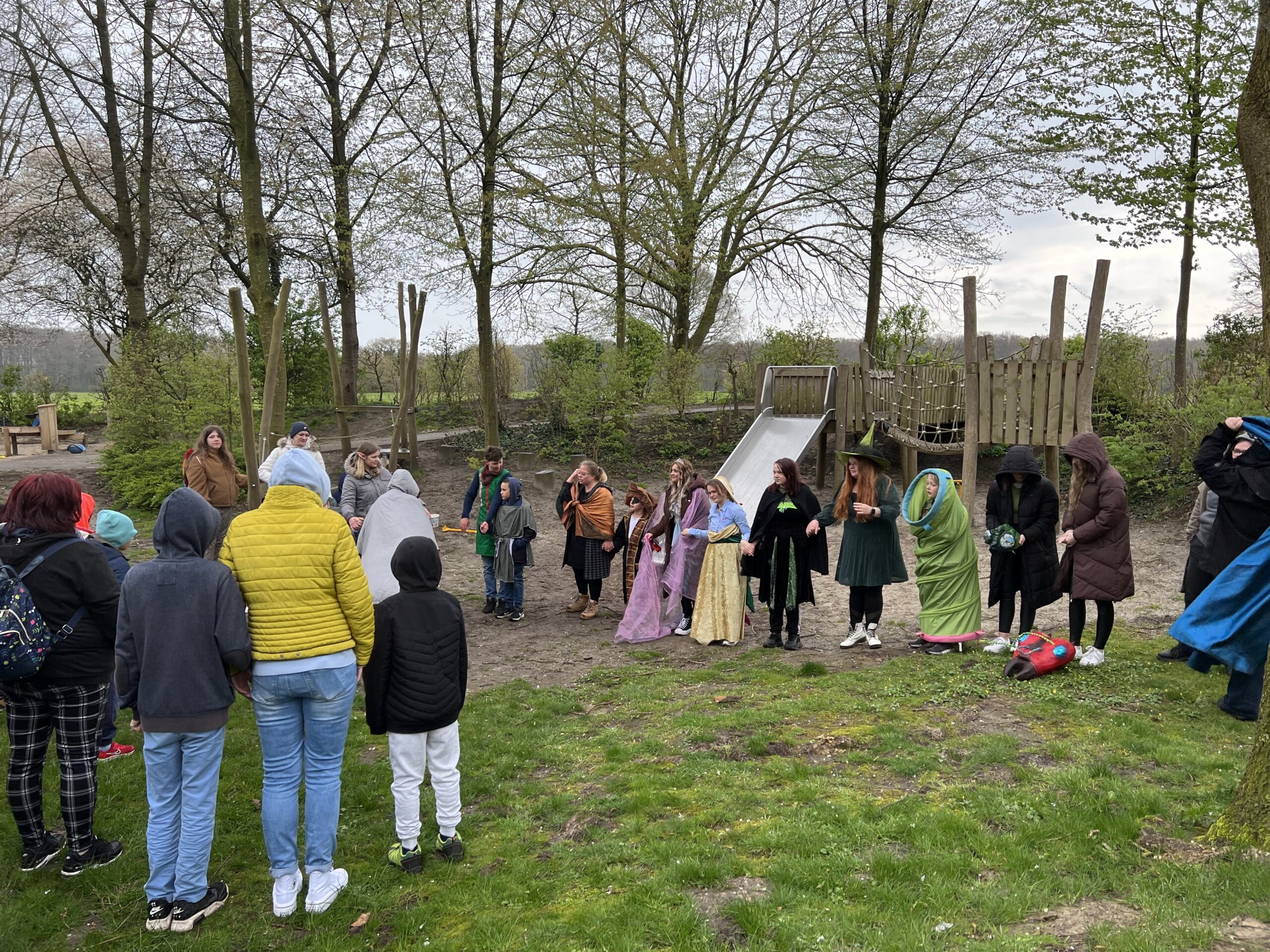 Viele junge Menschen sind draußen auf einem Spielplatz. Sie sind alle mit unterschiedlichen Kostümen für ein Theaterstück verkleidet.