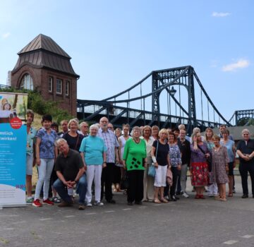 Eine Gruppe von Ehrenamtlichen und GPS Mitarbeiter sind draußen auf einem Parkplatz beim Südstrand. Im Hintergrund sieht man die Kaiser-Wilhelm-Brücke.