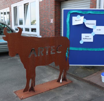 Draußen vor dem Eingang der GPS ARTEC Roffhausen steht ein selbst gebauteter Stier aus Metall. Neben dem Stier ist eine Infotafel, wo daran auf Zetteln steht "Herzlich Willkommen in der Artec Roffhausen".