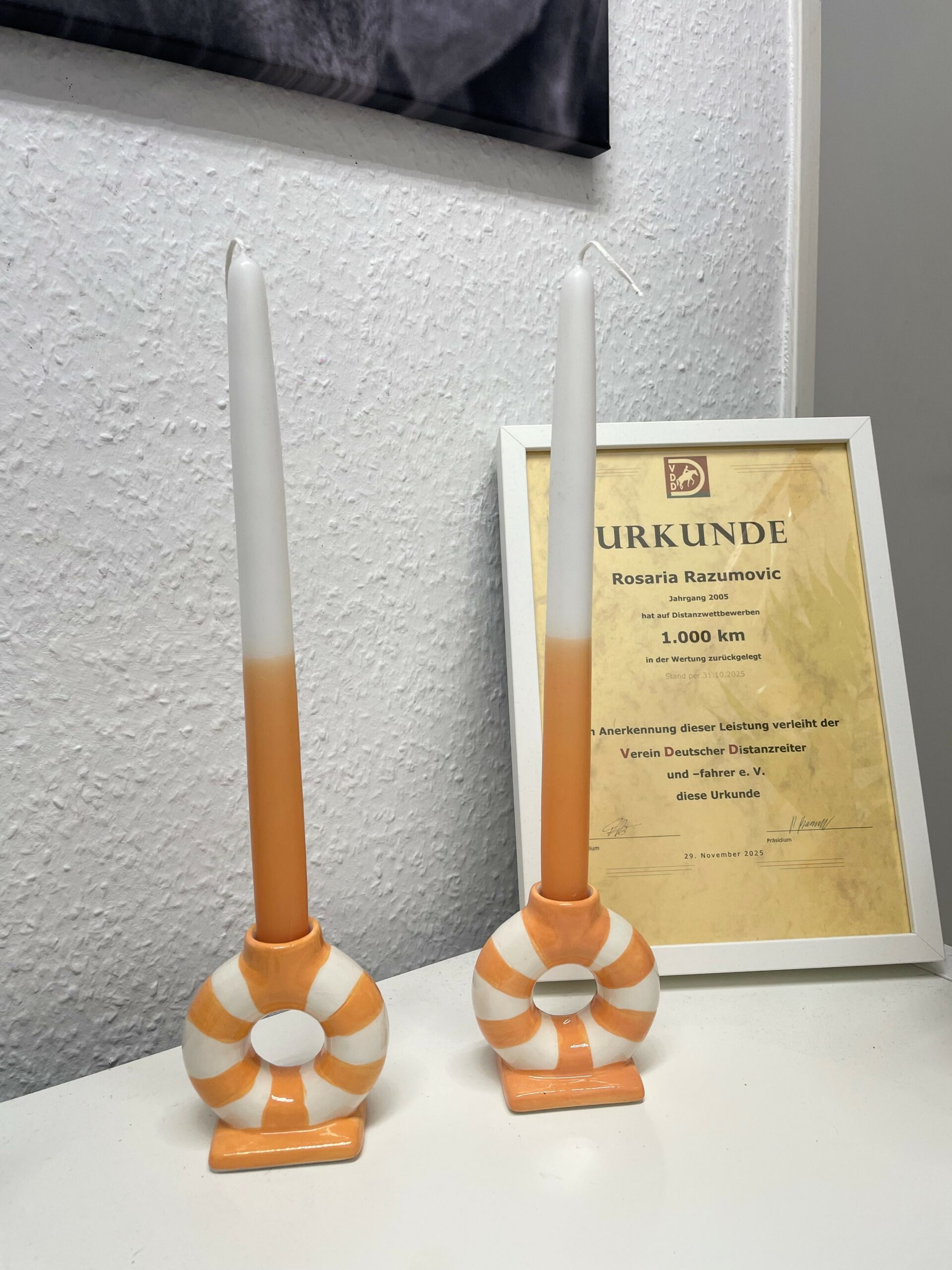 Zwei bunte Kerzen und eine Urkunde in einem Bilderahmen auf einem Tisch in einem Raum.